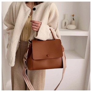 Brown leather handbag with a wide geometric patterned shoulder strap on a model