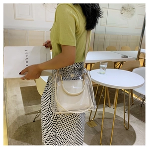 Close-up of clear PVC tote with white leather insert and gold handles in cafe setting