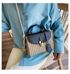 Detail of straw woven bag with black leather flap, gold lock and small white flower charm
