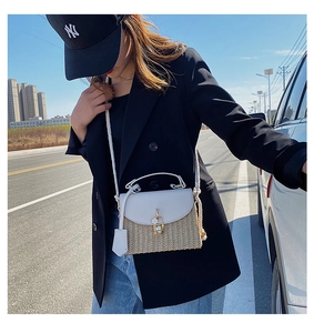 Detail of straw crossbody bag featuring leather flap, metal lock and thick rope shoulder strap
