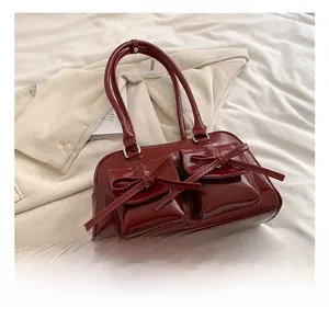Detail of dark red patent leather bag with glossy finish and ribbon bow accents