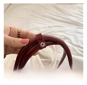 Close-up of wine red glossy leather handbag featuring comfortable handles and metal snap