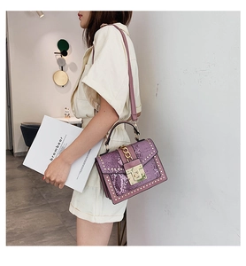 Side view of model carrying a purple sequined small square bag with gold rivet details