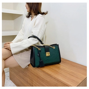 Detail of dark green crocodile texture handbag with gold metal lock and chain strap