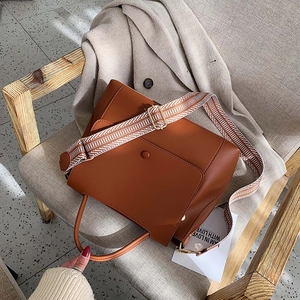 Caramel leather shoulder bag with wide geometric jacquard strap on a wooden chair