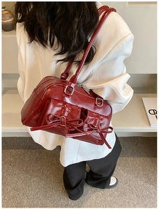 Detail view of deep red patent leather shoulder bag with decorative bow pockets
