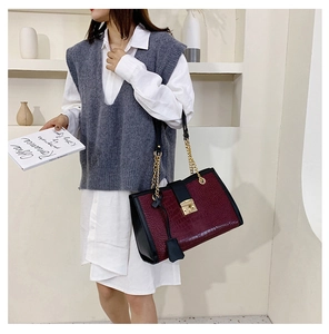 Detail of burgundy crocodile pattern texture and gold metal buckle on tote bag