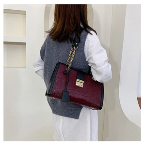 Detail of dark burgundy crocodile pattern tote bag with gold chain strap on model