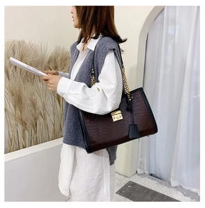 Detail of dark brown crocodile embossed tote bag with gold chain strap on a model