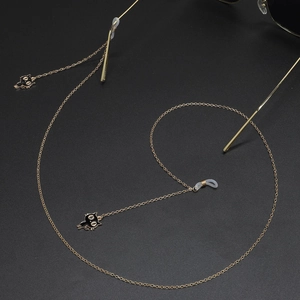 Chaîne de lunettes dorée avec pendentif chat noir en émail sur un fond de texture noire
