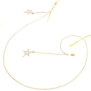 Chaîne à lunettes dorée en métal avec étoiles ajourées et petites perles sur fond blanc