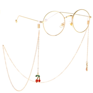 Goldene Brillenkette aus Metall mit roten Kirsch-Anhängern und runder Metallbrille auf Weiß