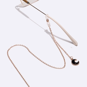 Detail of gold eyewear chain featuring black enamel moon and star pendant and rubber loop