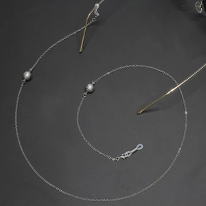 Chaîne à lunettes en métal argenté avec billes mates sur fond noir texturé