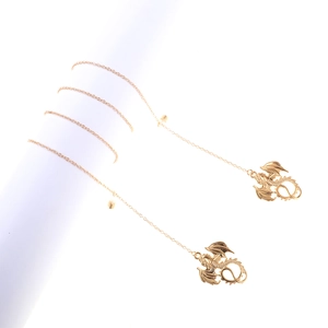 Détail de boucles d'oreilles dragon doré avec fine chaîne sur présentoir blanc