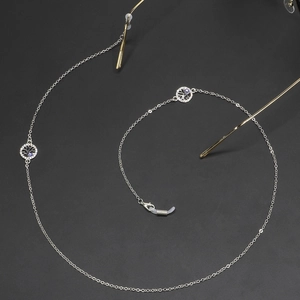 Silver eyeglasses chain with rhinestone Tree of Life and Evil Eye pendants on black surface