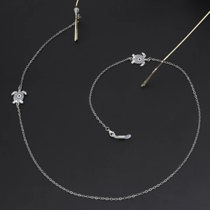 Silver eyeglasses chain featuring hollow turtle charms with white patterns on black background