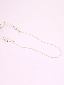 Detailed close-up of white pearl eyewear chain with gold clips on purple fabric