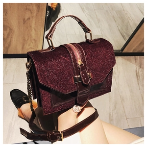 Nahaufnahme der weinroten Lackledertasche mit Glitzerstruktur und goldenem Metallgriff