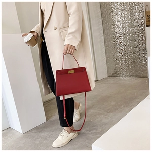 Détail du sac Kelly en cuir rouge avec boucle dorée porté par un mannequin
