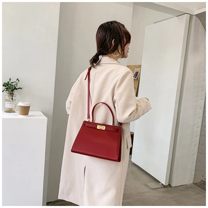 Vue détaillée d'un sac à main rouge en cuir texturé porté avec un trench-coat beige élégant
