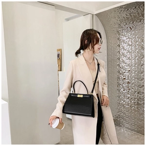 Sac à main chic en cuir noir avec fermoir doré porté par un mannequin