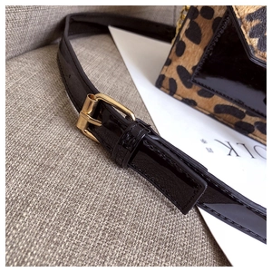 Detail eines glänzenden schwarzen Lederriemens mit Gold-Schnalle an einer Leo-Tasche