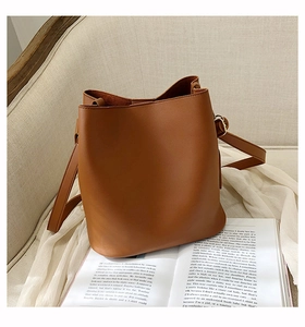 Detail of caramel brown matte PU leather bucket bag with adjustable strap on a soft sofa