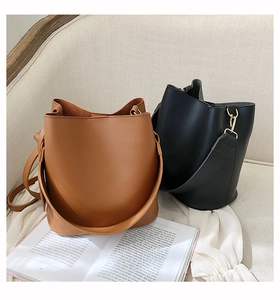 Detailed view of minimalist brown and black leather bucket bags on a beige sofa