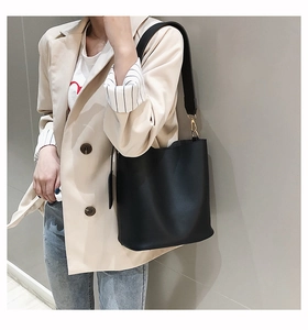 Detail view of black leather bucket bag with gold metal hook and wide shoulder strap