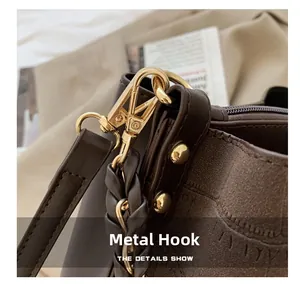 Close-up of golden metal lobster clasp and braided leather strap on a brown bucket bag