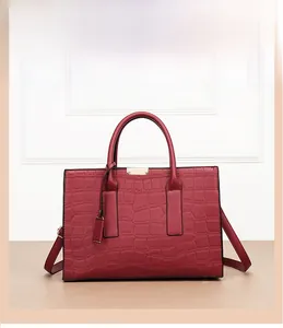 Detail of red crocodile texture handbag with gold metal clasp and dual handles