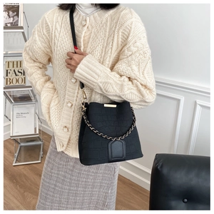 Close-up of black crocodile pattern bucket bag with gold chain and metal bar details