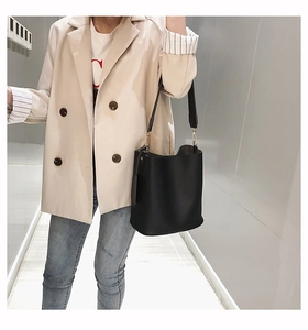 Detail of a large black leather bucket bag styled with a blazer and denim jeans