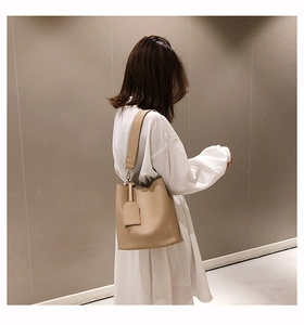Detailed side view of a beige leather bucket bag worn by model with wide strap