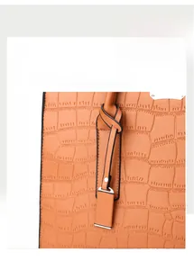 Detail of bright orange crocodile embossed leather handbag with knotted handle and gold hardware