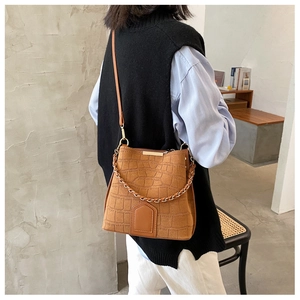 Detailed shot of brown crocodile pattern bucket bag with chain strap worn by a model