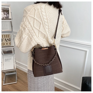 Detail of dark brown faux crocodile bucket bag with metal chain on a beige sweater