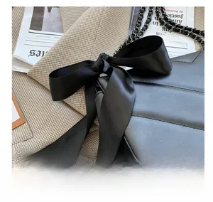 Detail of black quilted shoulder bag featuring a large silk bow and silver metal chain strap
