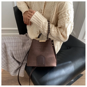 Detail of dark brown faux-leather bucket bag with crocodile texture and metal chain