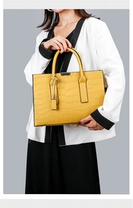 Model posing with yellow crocodile embossed leather handbag over black and white suit