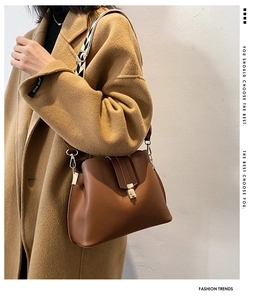 Detail of caramel brown leather bucket bag with geometric patterned wide strap and gold buckle