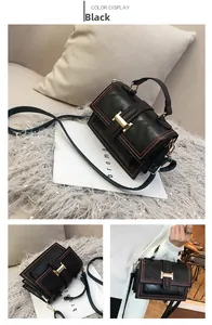 Detail of black crossbody bag featuring gold H-shaped hardware and red contrast stitching