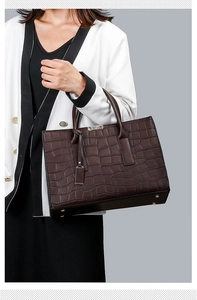 Detail of dark brown crocodile embossed tote bag with metal feet on light grey background