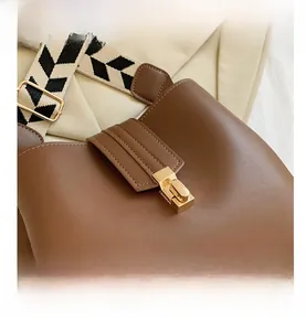 Close-up of brown litchi pattern leather bag with gold lock and geometric strap