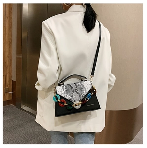 Detail of snake pattern crossbody bag with acrylic chain worn by a model in a white blazer