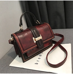 Close-up of vintage burgundy satchel with textured finish and gold metal buckle detail