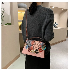 Detail of pink crossbody bag with snake print flap and resin chain worn by a model