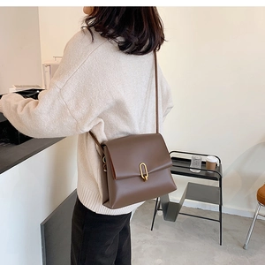 Brown matte leather shoulder bag with gold oval lock shown in a cafe lifestyle setting