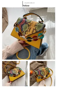 Detail of yellow crossbody bag featuring snake print flap and chunky acrylic chain strap